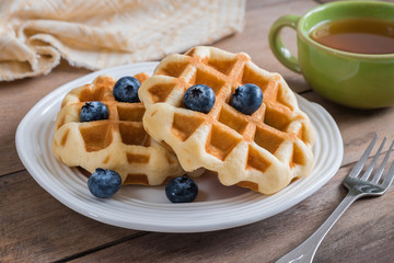 Waffle with blueberry on plate and cup of tea