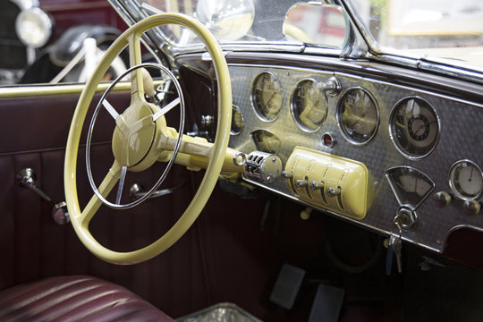 Isolated View Vintage Automobile Chrome Dashboard, Yellow Steering Wheel, Red Leather Seats, Out of Focus Autos in Background