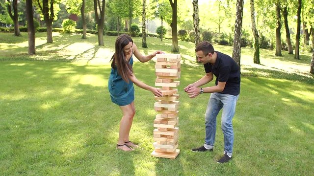 Pair of young people plays big game from large blocks in a Park. Active logic outdoor games. Slow motion.