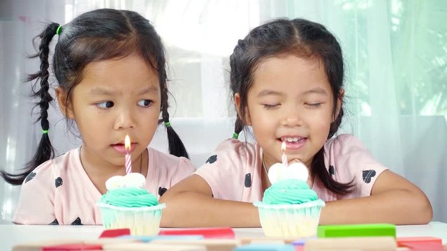 Two asian little girl blows out candles on birthday cake together in house