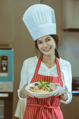 Female chef holding prepared dish in kitchen for cooking spaghetti Pad Kee Mao Seafood menu, Thai Food