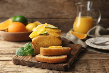 Cutting board with delicious sliced citrus cake and fruits on wooden table