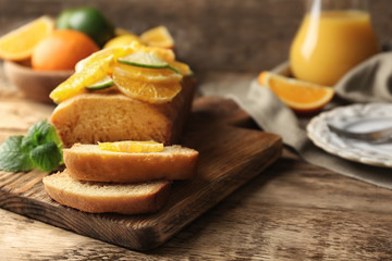 Cutting board with delicious sliced citrus cake and fruits on wooden table