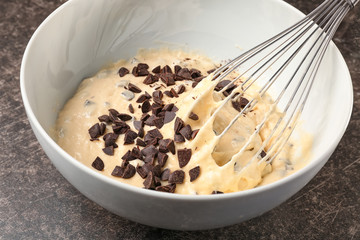 Bowl with raw dough and chopped chocolate chips on kitchen table