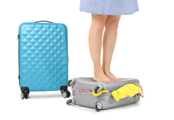 Young woman trying to pack her luggage on white background. Luggage overweight concept