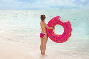 Naklejka na ściany i meble Beautiful young woman with colorful inflatable donut at sea coast