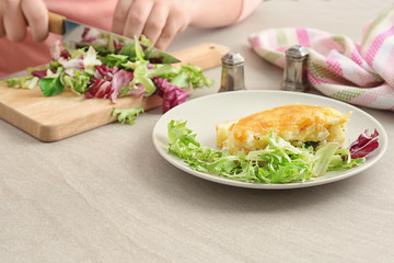 Woman cutting mixed salad for tasty casserole in kitchen