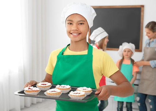 African American boy holding tray with delicious cakes prepared during cooking classes
