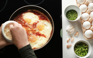 Female hand pouring parmesan cheese on eggs in purgatory