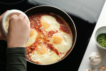 Female hand pouring parmesan cheese on eggs in purgatory