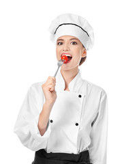 Young female chef eating tomato on white background