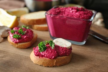 Sandwiches with square glass bowl of delicious beet hummus on wooden board