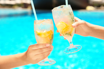 Young women with glasses of lemonade near swimming pool