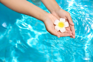 Young woman holding flower over blue clean water in swimming pool. Spa concept