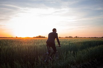 Fototapeta na wymiar A caucasian businessman riding a bicycle in summer fields, Male in business suit ride on fixie bike.