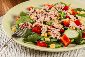 Fresh spinach salad with tuna, cucumber, corn, and red paprika on a plate