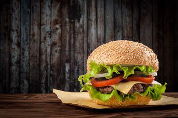 Delicious cheeseburger with salad ingredients on a grilled beef patty on a rustic wooden table with...