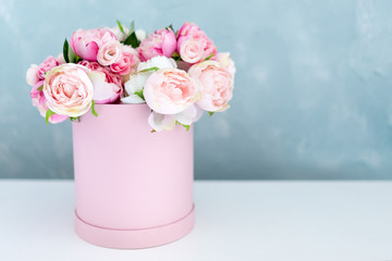 Flowers in round luxury present box. Bouquet of pink and white peonies in paper box. Mock-up of hat box of flowers with free copyspace for text. Interior decoration in in pastel colors.