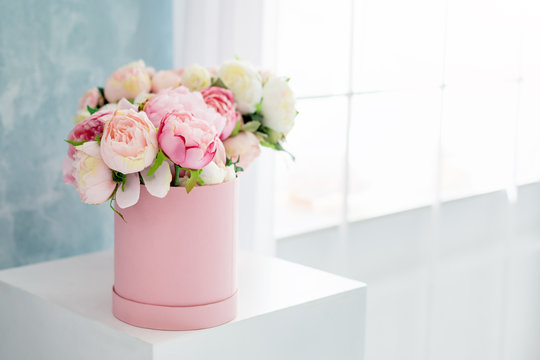 Flowers in round luxury present box. Bouquet of pink and white peonies in paper box near the window.Mock-up of hat box of flowers with free copyspace for text. Interior decoration in in pastel colors.