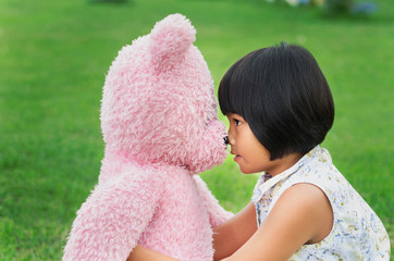 little girl is good friend with  teddy bear and sitting at the playground at the park