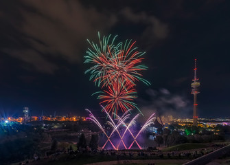 Buntes, spektakuläres Feuerwerk über der Stadt München im Olympiapark mit farbigen Raketen neben...