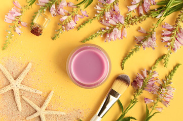 Obraz na płótnie Canvas Herbal essence. Botanical summer skincare. Violet flowers and facial mask in jar with application brush, bright yellow background with starfish and sand. 