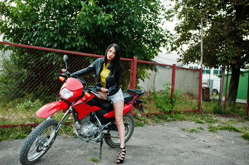 Portrait of a cool and awesome woman in dress and black leather jacket sitting on a cool red motorbike.