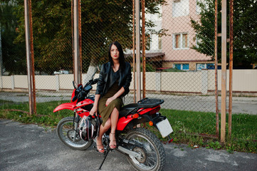Fototapeta na wymiar Portrait of a cool and awesome woman in dress and black leather jacket sitting on a cool red motorbike.