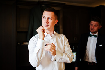 Groom dressing up in the presence of his groomsmen in the room.