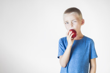 Portrait happy, smiling boy eats an red apple. Funny child holding an apple. Looking at camera. The concept of a healthy lifestyle, organic vegetarian food.