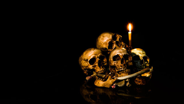 The visual art still life image of human skulls and pile bone with candle Light