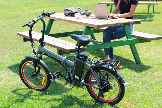 Women with electric Bicycle and laptop sitting in the park