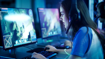 Professional Girl Gamer Plays in MMORPG/ Strategy Video Game on Her Computer. She's Participating in Online Cyber Games Tournament, Plays at Home, or in Internet Cafe. She Wears Gaming Headset. - obrazy, fototapety, plakaty