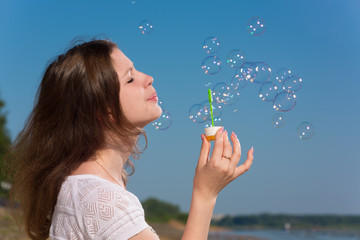 Girl inflates soap bubbles on blue sky background
