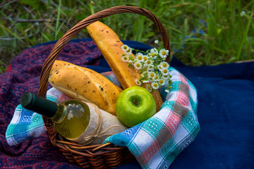 Picnic basket with white wine, two baguettes, green apple and a bunch of chamomiles in nature