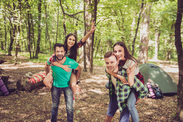 Close up of a four cheerful funky friends tourists. Camp in the sunny wood, tent and backpacks. Two...