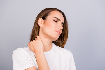 Obraz premium Young frustrated brown haired lady is having a strong pain in neck. She is in a white tshirt, massaging the neck, with pain grimace