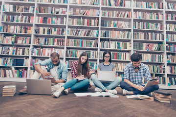 Low angle shot of four international clever bookworms students in the library studying, sitting...