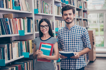We like education! Successful future for smart youth! Two attractive young bachelors are welcoming in their university`s library`s archive, holding literature, smiling, wearing casual smart