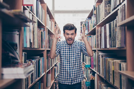 Going crazy and insane, psycho and agression. Shouting stressed young brunet bearded student is blasting standing between the book shelves in the library