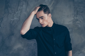 Young fashionable guy in black shirt touching his hair and posing against gray background