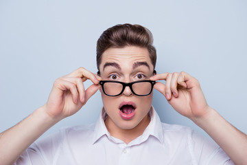 Close up portrait of wondered and shocked young handsome guy in white shirt touching his glasses with wide open eyes and mouth