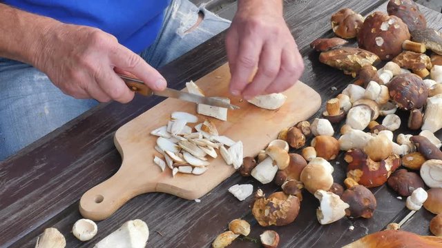 Chop fresh wild mushrooms. Close up shot of hands with a knife cutting mushrooms. Man hand carefully  cut wild mushrooms on a kitchen wooden board 