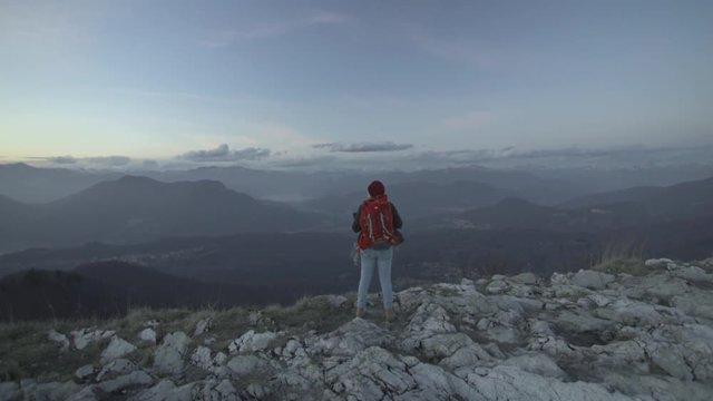 Ragazza con zaino arriva in cima alla montagna e osserva il panorama