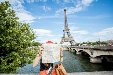 Young woman tourist sitting with paper map in front of the Eiffel tower in Paris