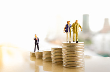 Concept of retirement planning. Miniature people: Old couple figure standing on top of coin stack.