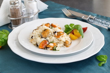 Risotto with mussels on a white plate with basil, cherry tomatoes on a green cloth. Healthy eating concept, Meditarranian life style.