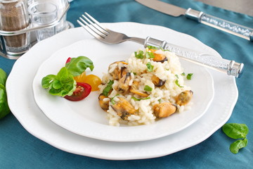 Risotto with mussels on a white plate with basil, cherry tomatoes on a green cloth. Healthy eating concept, Meditarranian life style.