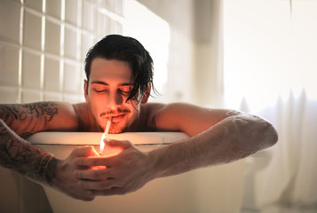 Attractive guy relaxing in the bathtub while smocking a cigarette