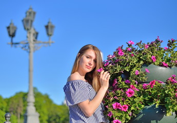 Beautiful girl standing near flower bed in front of an ancient street lamp